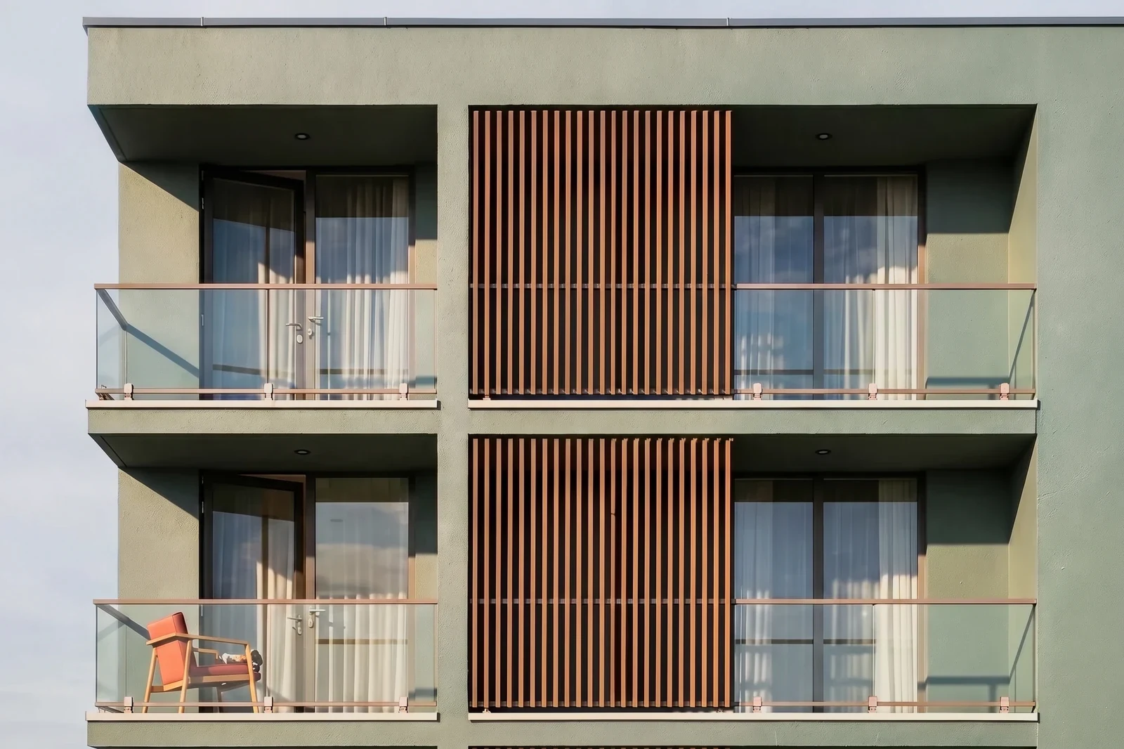 A contemporary apartment building seen head on. Two floors of balconies behind glass railings, with timber screens between them.